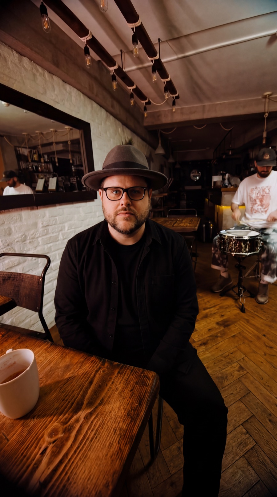 Grant Morriss seated in a café with a drummer behind him